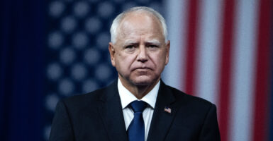 Walz stares grimly at the camera with a U.S. flag hanging behind him.