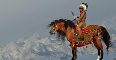 An American Indian sits on his Appaloosa horse on a high cliff in a desert area.