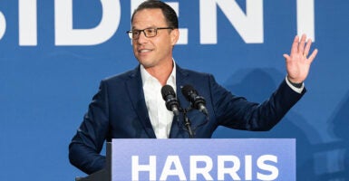 Josh Shapiro in a blue suit raises his hind behind a podium reading 