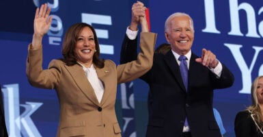 Kamala Harris in a tan coat holds hands with Joe Biden in a black suit