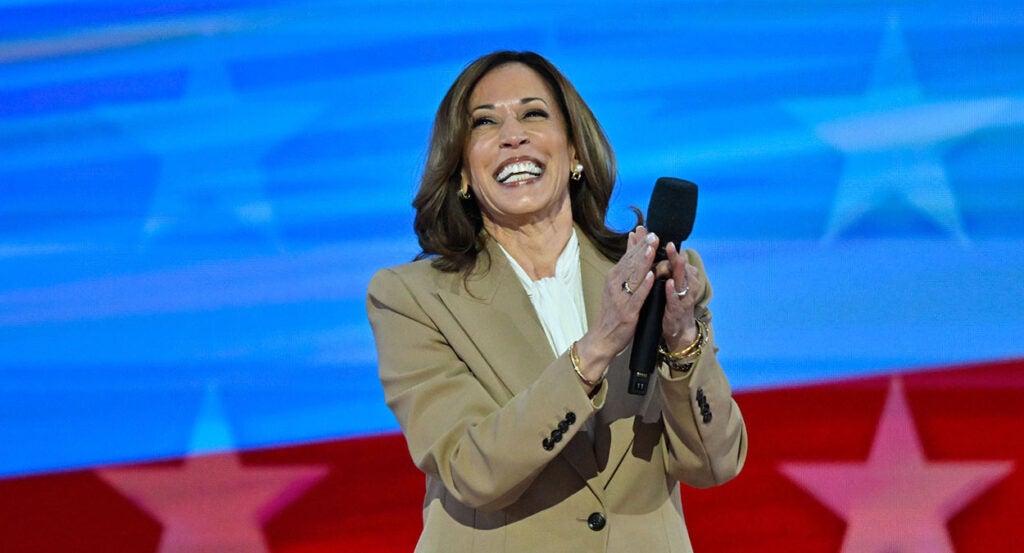 Kamala Harris in a tan suit coat claps her hands and laughs