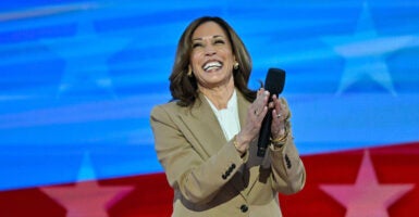 Kamala Harris in a tan suit coat claps her hands and laughs