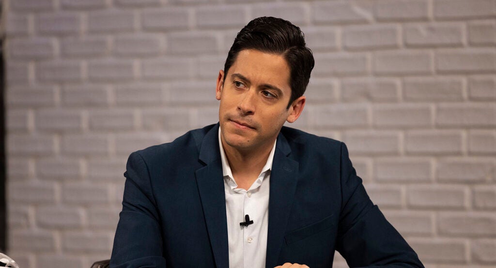 Michael Knowles in a black sport coat and a white shirt stares intently