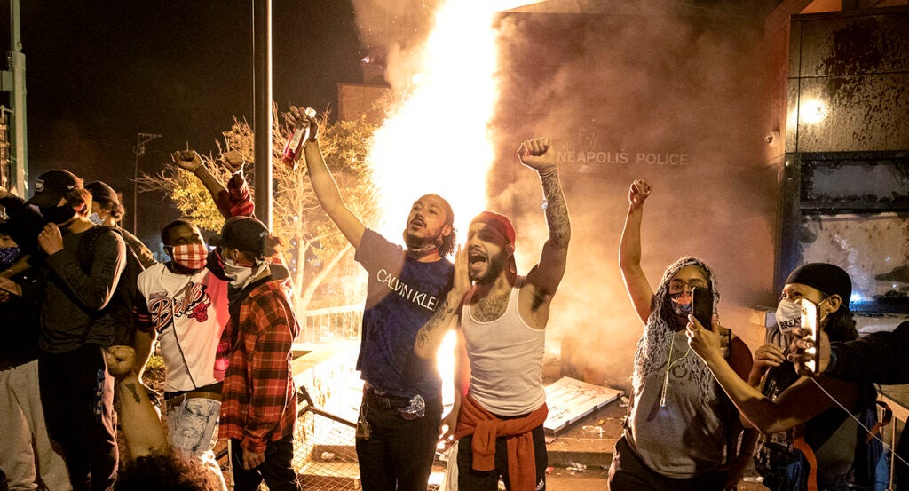 Rioters raise fists in front of the Minneapolis police station as it burns