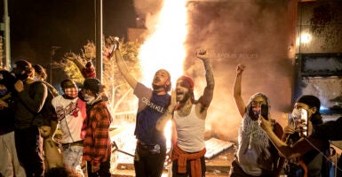 Rioters raise fists in front of the Minneapolis police station as it burns