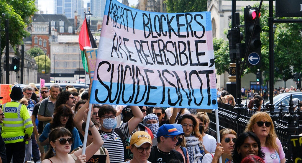 Protesters hold a sign reading, "Puberty Blockers Are Reversible, Suicide Is Not."