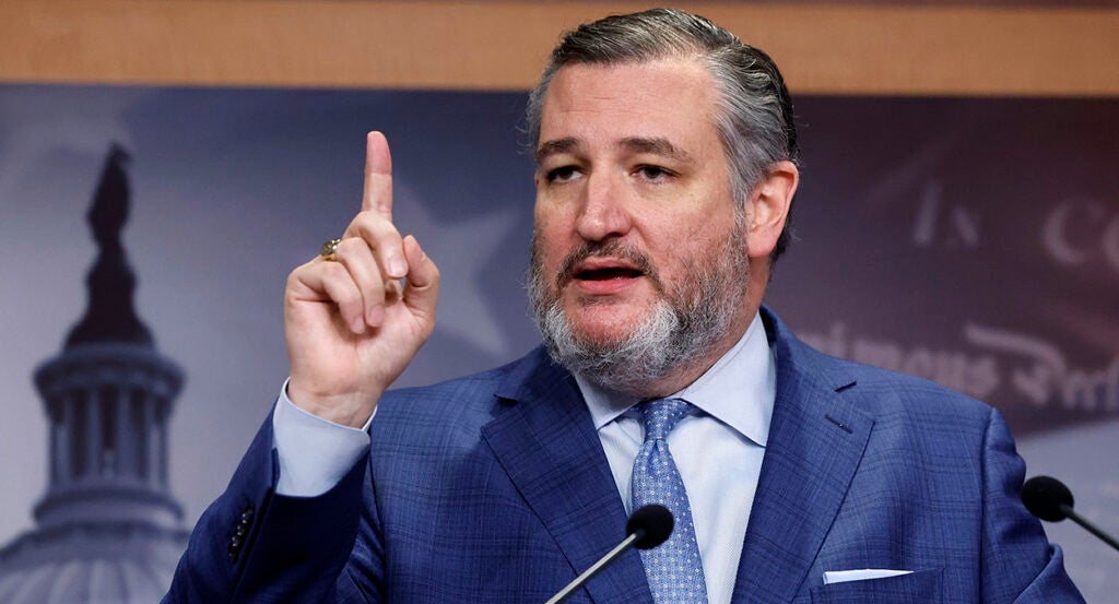 Ted Cruz, in a blue suit with a blue tie, raises his finger in front of a picture of the U.S. Capitol