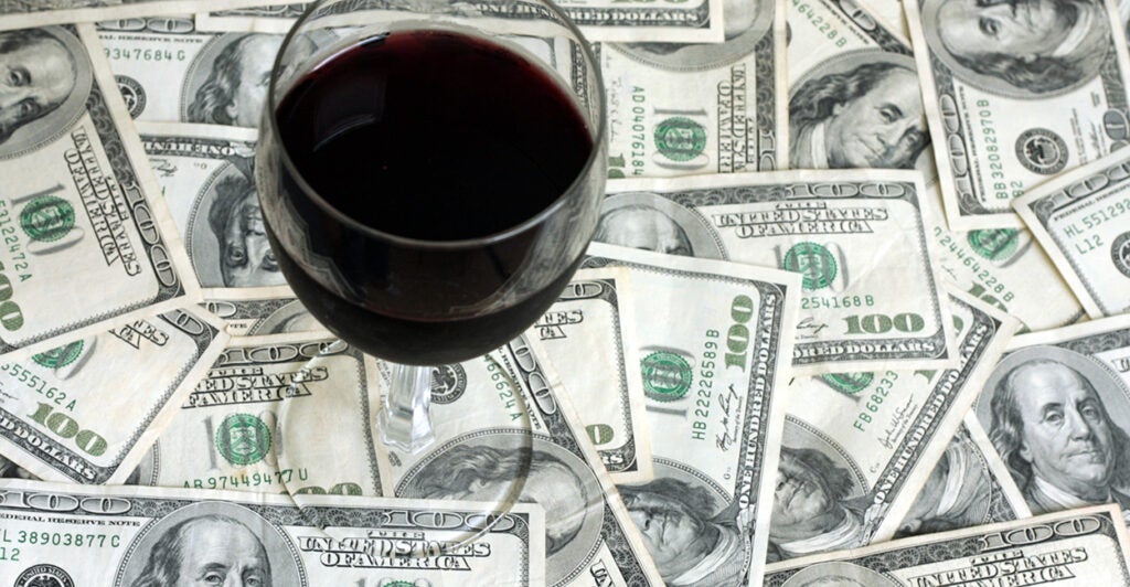 A glass of red wine sitting atop scattered $100 bills