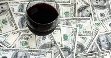 A glass of red wine sitting atop scattered $100 bills