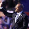 Colin Allred waves while wearing a black suit and a light blue tie