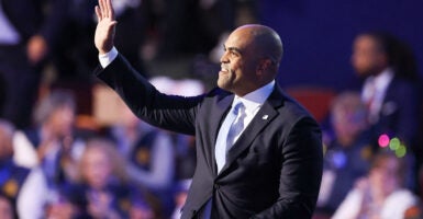 Colin Allred waves while wearing a black suit and a light blue tie