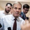 Jim Jordan in blue shirt and red tie taking questions from reporters