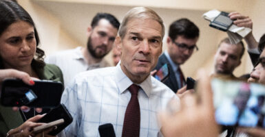 Jim Jordan in blue shirt and red tie taking questions from reporters