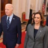 President Joe Biden in a blue suit walks with Vice President Kamala Harris in a grey suit in the White House