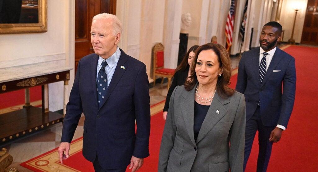 President Joe Biden in a blue suit walks with Vice President Kamala Harris in a grey suit in the White House