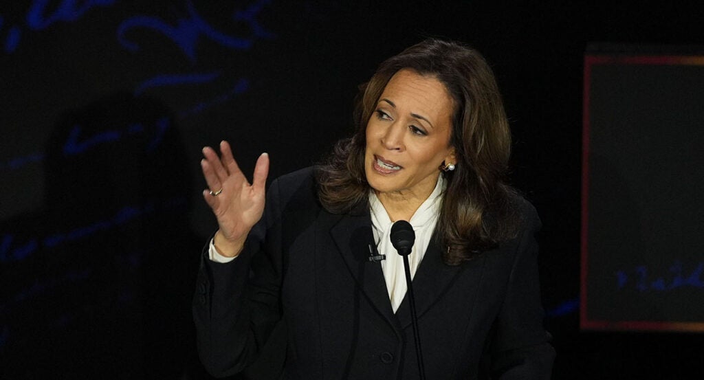 Kamala Harris in a suit leans left, gesturing