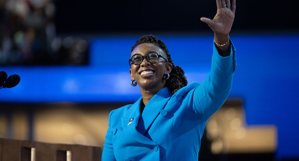 Kelley Robinson in a blue suit raises her hand