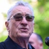 Robert DeNiro wears sunglasses and stands at a microphone