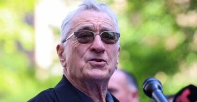 Robert DeNiro wears sunglasses and stands at a microphone