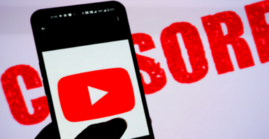 The YouTube logo is displayed on a smartphone with the word “CENSORED” displayed in the background.