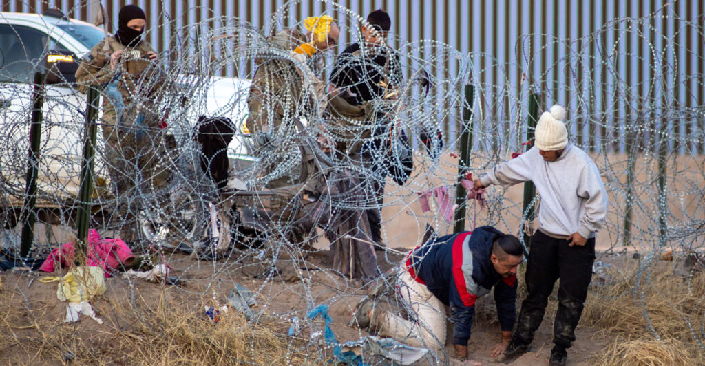 Five illegal immigrant men trying to climb under razor wire at the US-Mexico border