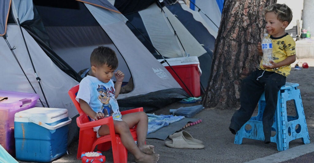 two small boys sitting outside in front of tents at a makeshift migrant shelter