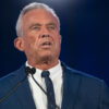 Robert Kennedy Jr. in a blue suit at a podium with a black background