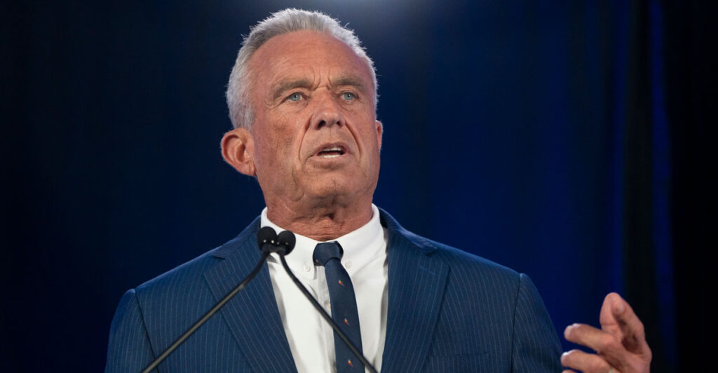 Robert Kennedy Jr. in a blue suit at a podium with a black background