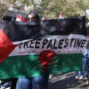 A woman marches with a sign reading "Free Palestine" with blood all over it