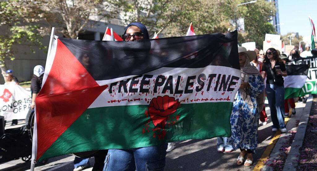 A woman marches with a sign reading "Free Palestine" with blood all over it