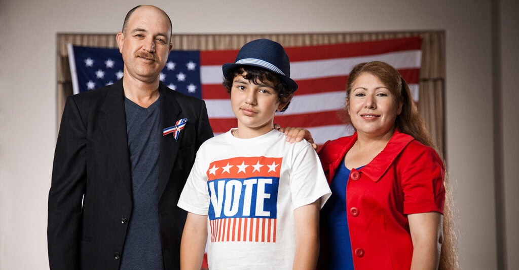 Smiling Hispanic family standing in polling place. (Hill Street Studios / Getty Images)