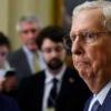 Mitch McConnell in blue suit surrounded by staff and reporters.