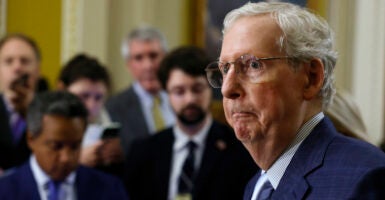 Mitch McConnell in blue suit surrounded by staff and reporters.