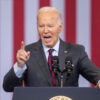 Joe Biden gestures angrily in a grey suit in front of an American flag