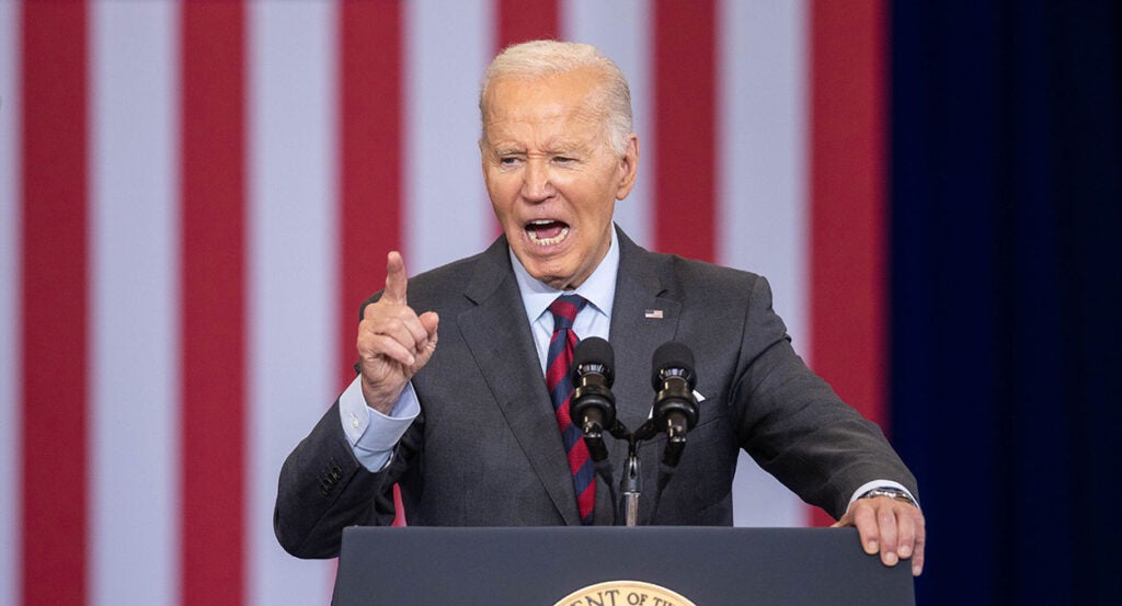 Joe Biden gestures angrily in a grey suit in front of an American flag