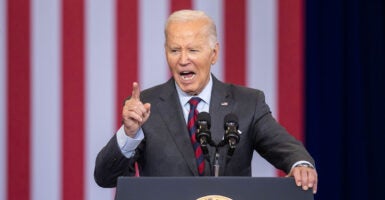 Joe Biden gestures angrily in a grey suit in front of an American flag