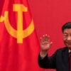 Chinese President Xi Jinping waves as he stands in front of a large Chinese flag