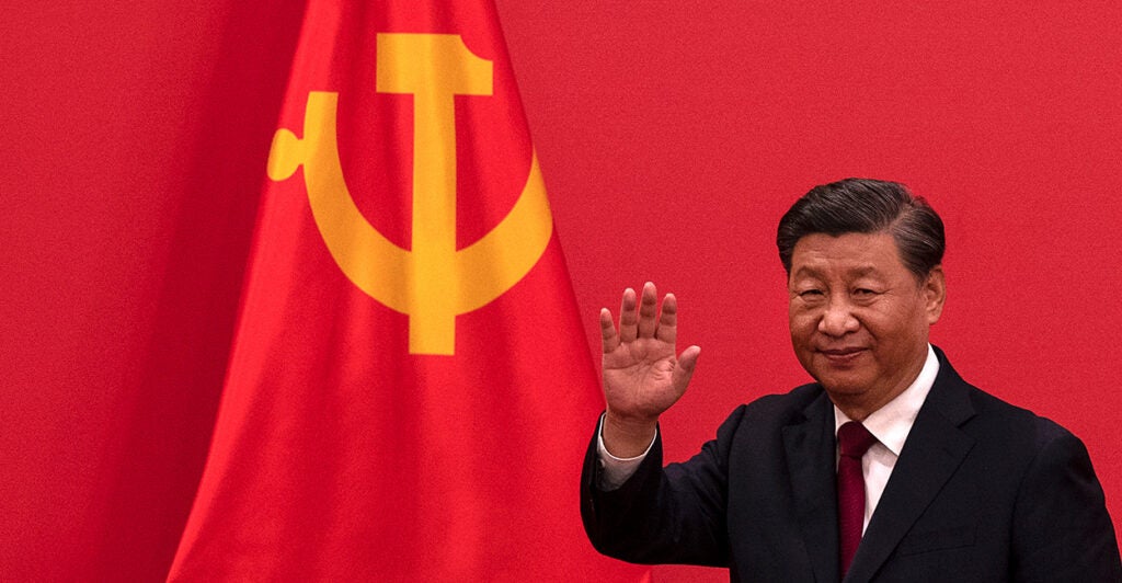 Chinese leader Xi Jinping waves as he stands in front of a large Chinese flag