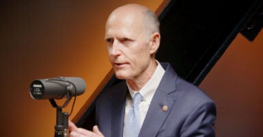 Rick Scott in a grey suit speaks in front of a microphone