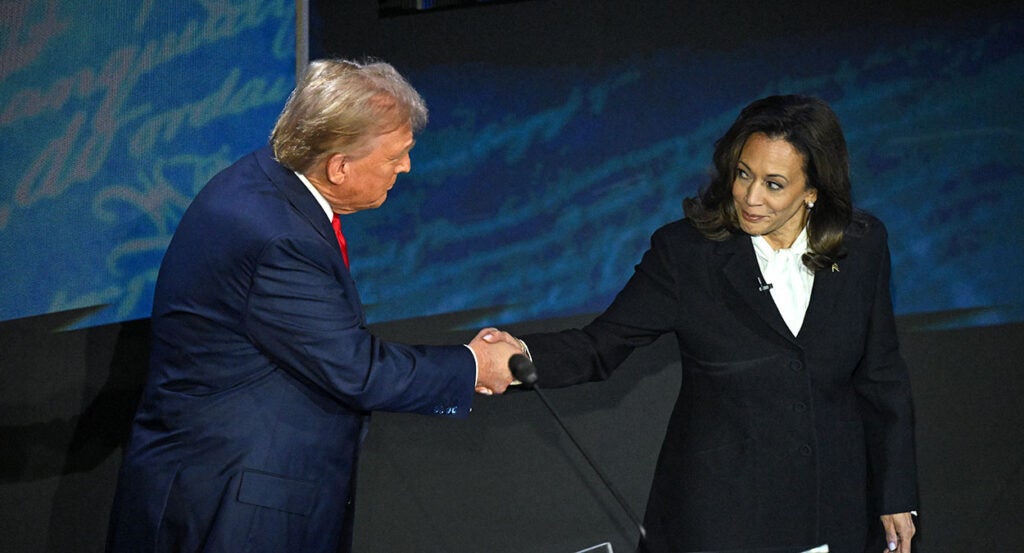 Donald Trump in a blue suit shakes hands with Kamala Harris in a black and white suit