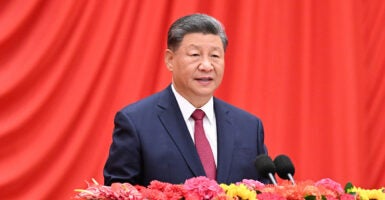 Chinese Premier Xi Jinping in a blue suit speaks in front of a red background with flowers in front of him