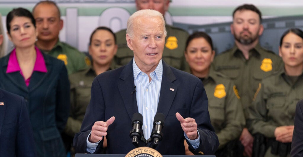 Joe Biden at a podium giving remarks in front of several uniformed border patrol officers