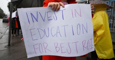 A woman holds a handwritten poster at a protest that says, 