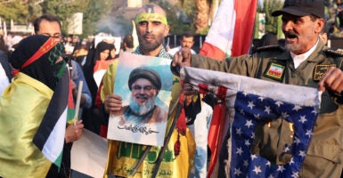 Iranian people in the streets protesting against the United States holding pictures of a slain Hezbollah leader and a burning American flag