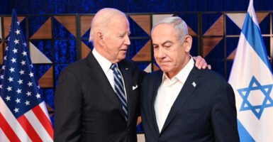 Joe Biden and Benjamin Netanyahu on stage In an embrace with American and Israeli flags behind them