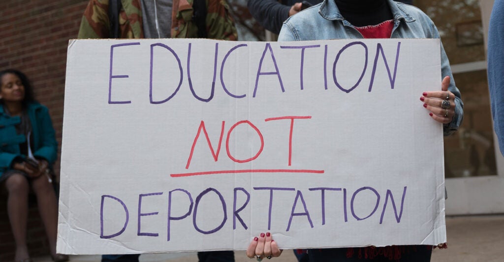 A student at a protest holding a handwritten sign saying, "education, not deportation."