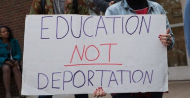 A student at a protest holding a handwritten sign saying, 