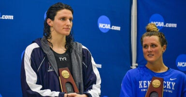 Biological male Lia Thomas dressed as a female swimmer standing next to Riley Gaines at a swimming championship