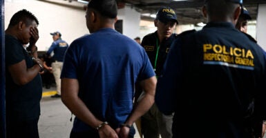 In a parking garage, the Guatemalan National Civil Police take handcuffed human traffickers to a court appearance