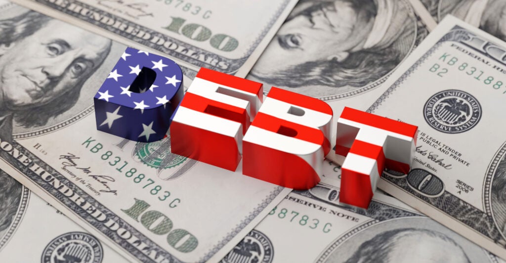 The word "debt" written in red, white, and blue atop a pile of $100 bills